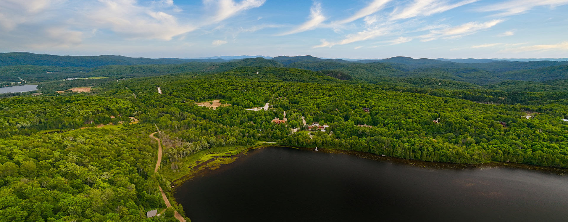 An aerial photo of a summer lake, surrounded by lush greenery in the background.