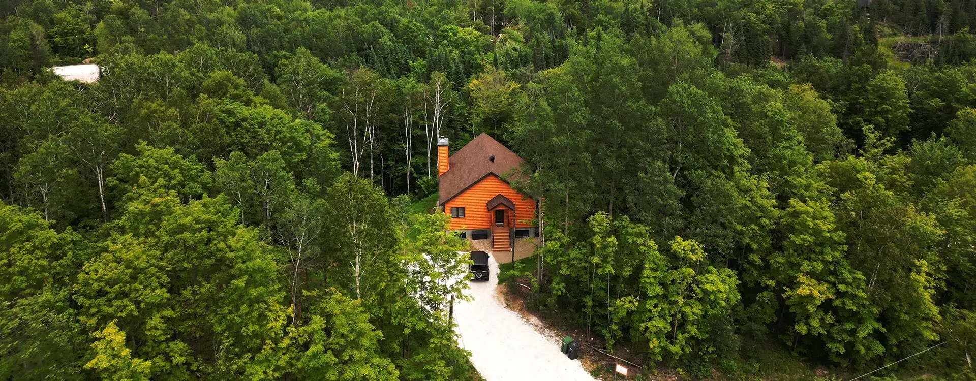 Photo aérienne d’un chalet entouré d’arbres verts en plein été.